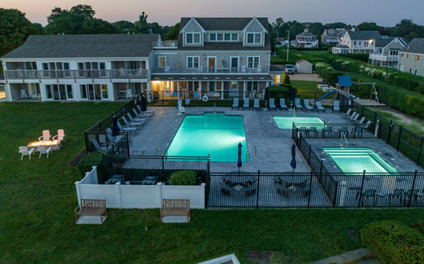 Beachside Village Resort’s illuminated pool area at dusk, featuring lounge chairs, umbrellas, and a hot tub surrounded by fencing.