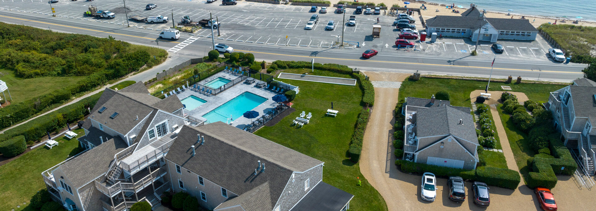 Aerial view of Beachside Village Resort showing the resort's swimming pool, parking lot, and beachfront location across the road.