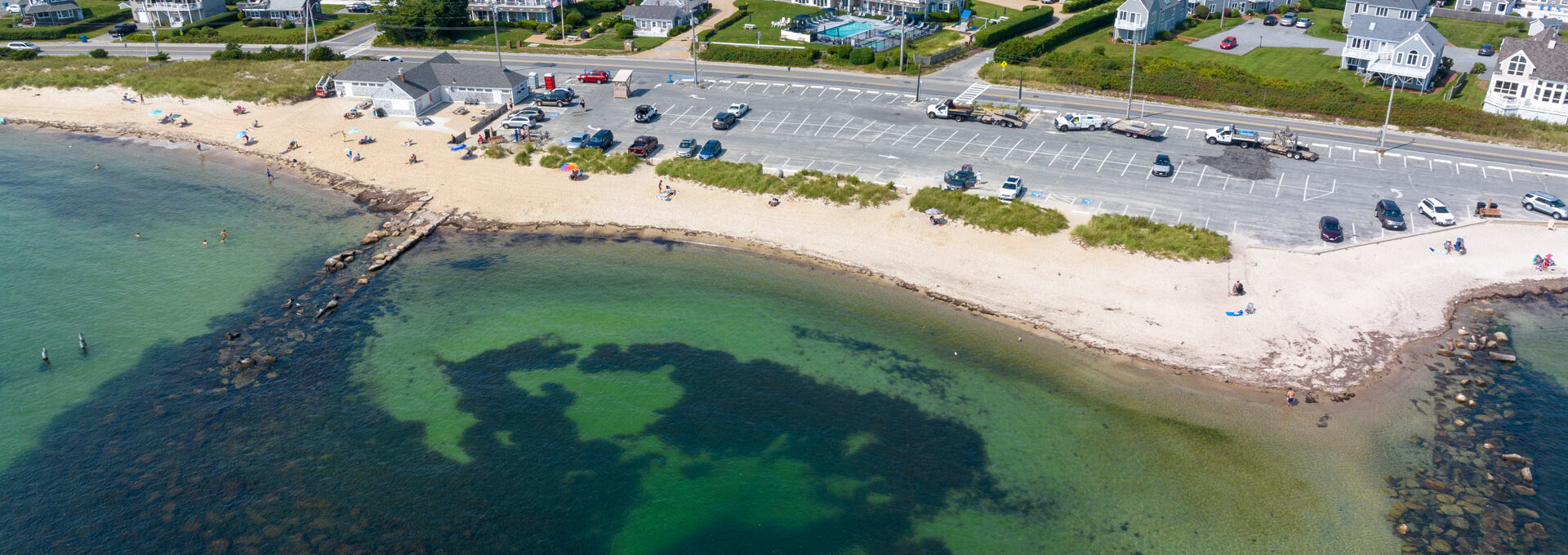 Aerial shot of Surf Drive Beach near Beachside Village Resort with calm waters, parking area, and sandy shore.