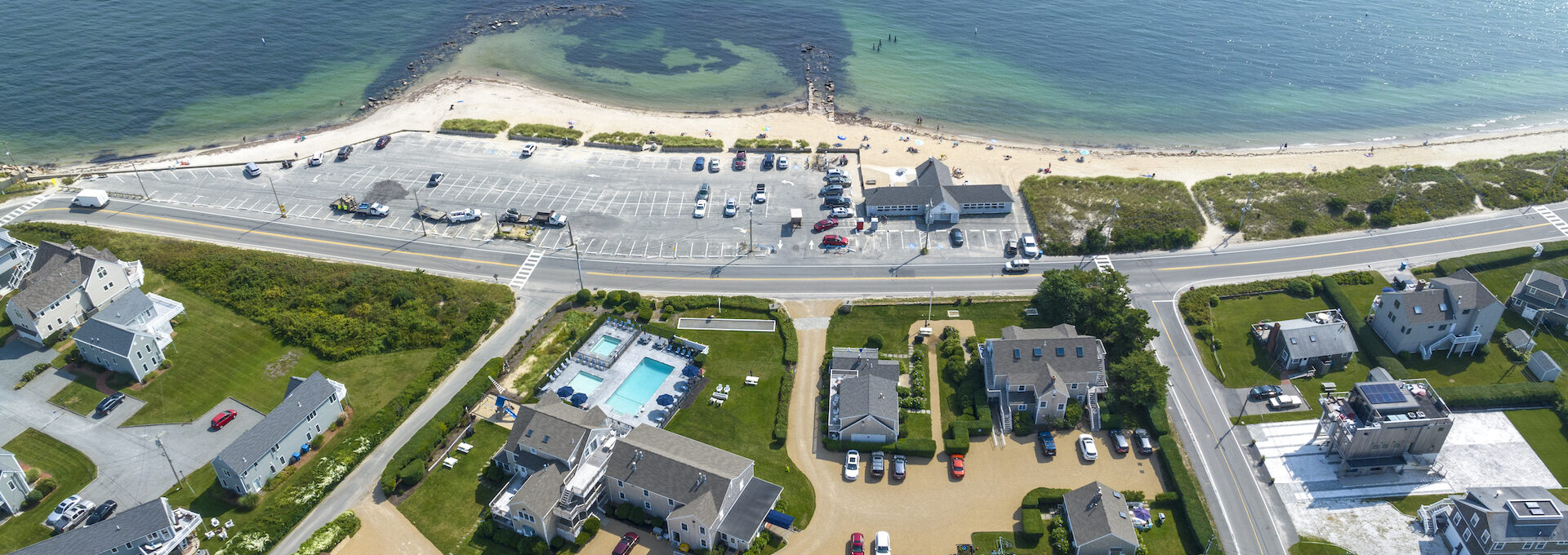 Aerial view of Beachside Village Resort with the main pool, surrounding green lawn, and the beach across the road.