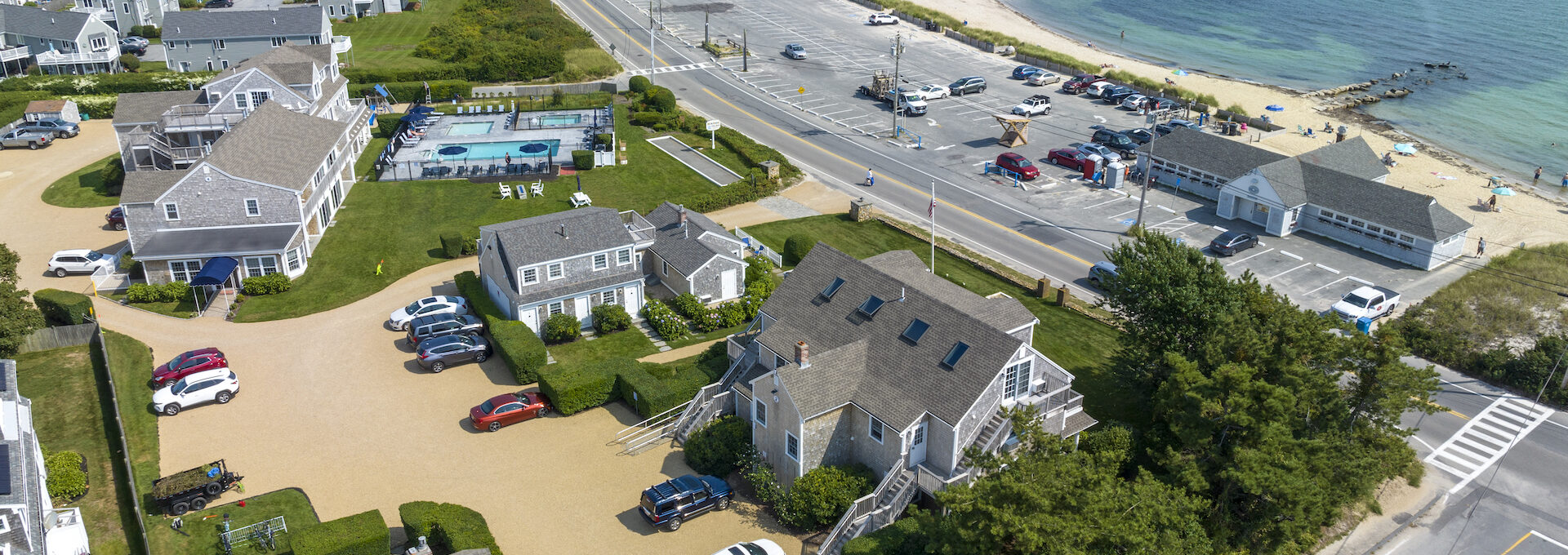 Aerial perspective of Beachside Village Resort showing parking areas, pool, and sandy beach with clear ocean waters.