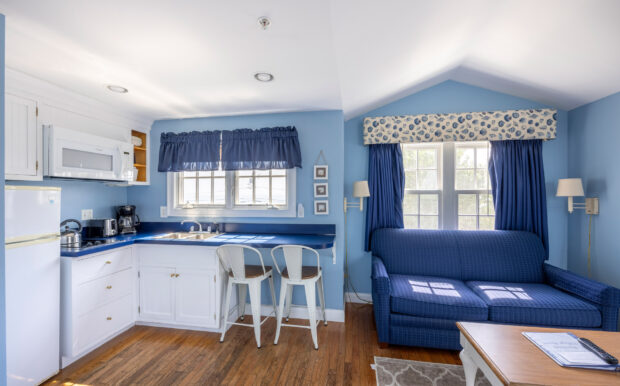 A wide-angle view of the studio with a kitchenette, navy sofa, white coffee table, and a bed under sloped ceilings.