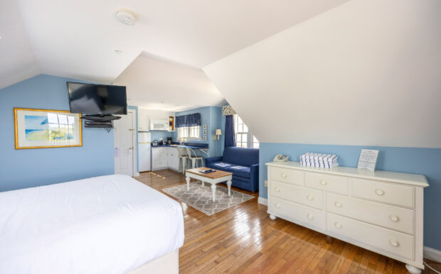 A cozy nook in the studio with a white kitchenette, bar seating, and a navy sofa next to large windows.